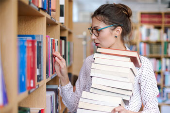 Soziale Arbeit Masterstudentin sucht nach Fachliteratur und trägt einen großen Stapel Bücher.