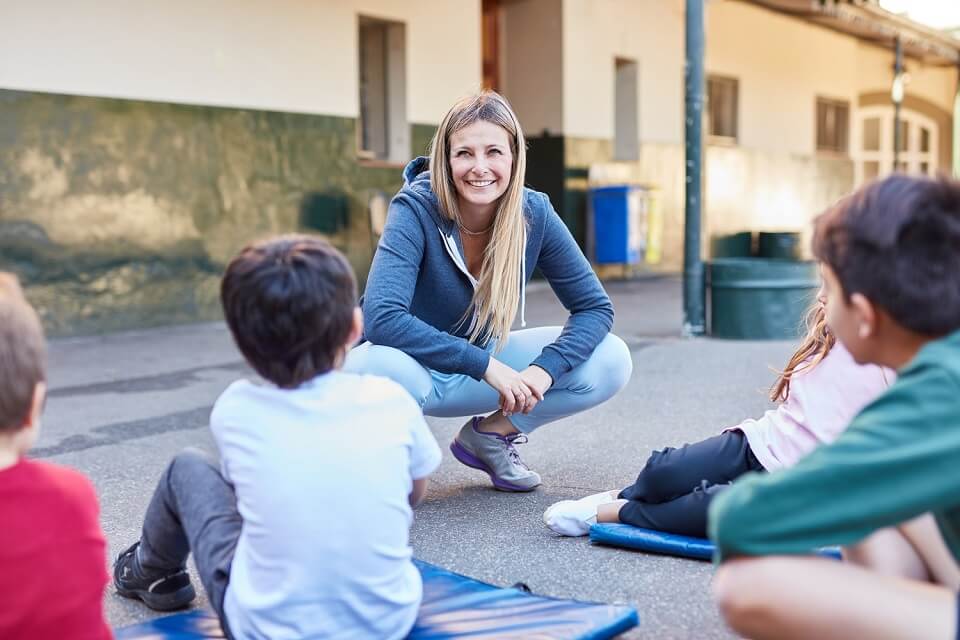 Studentin sitzt mit Kindern auf dem Pausenhof
